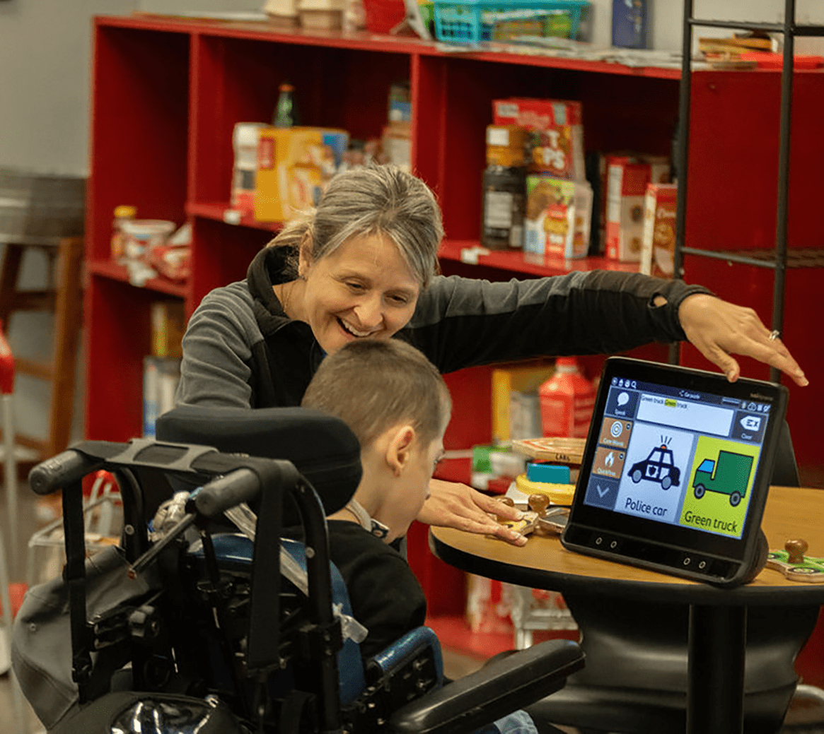 Julie, Elite Therapy Center SLP, works with a child using an AAC device.